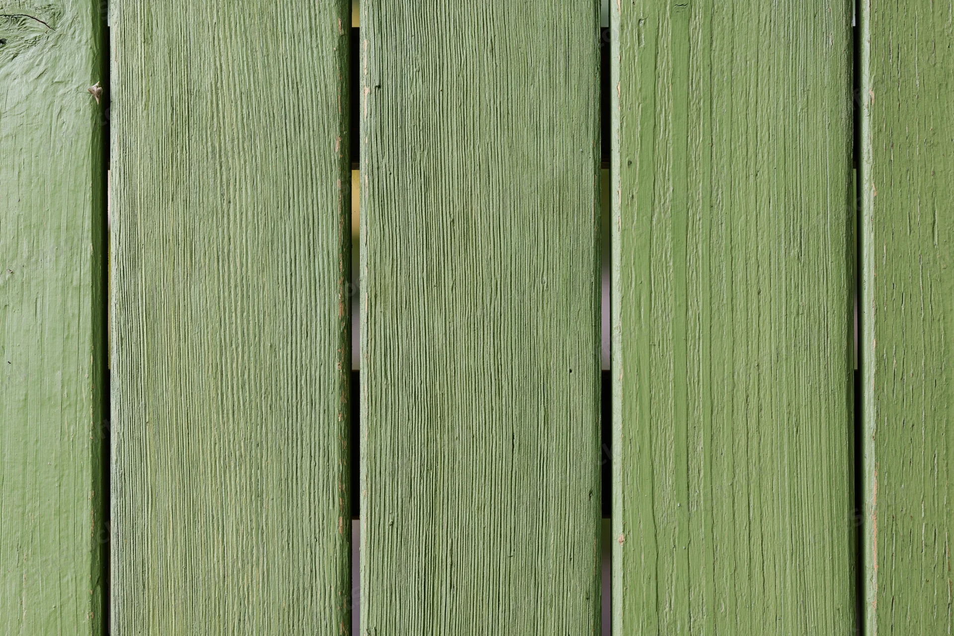 Vertical green painted wooden planks showing weathered texture and grain as part of an outdoor fence