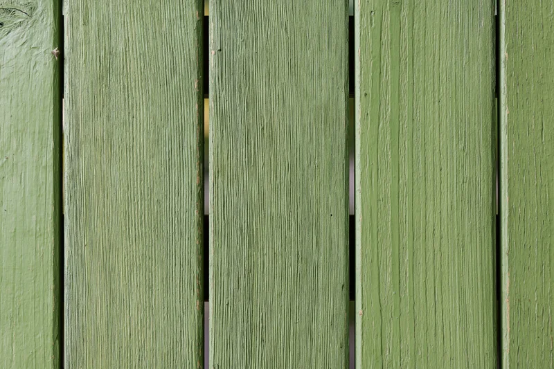 Vertical green painted wooden planks showing weathered texture and grain as part of an outdoor fence