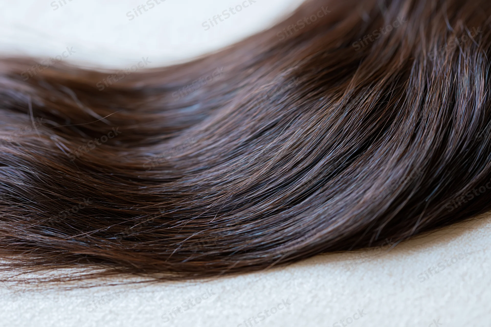 Close-up of dark brown hair extension lying on a light surface