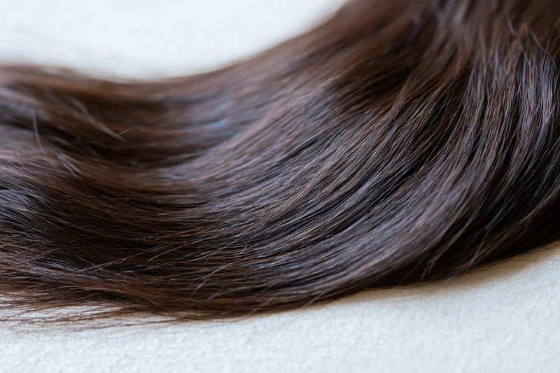 Close-up of dark brown hair extension lying on a light surface