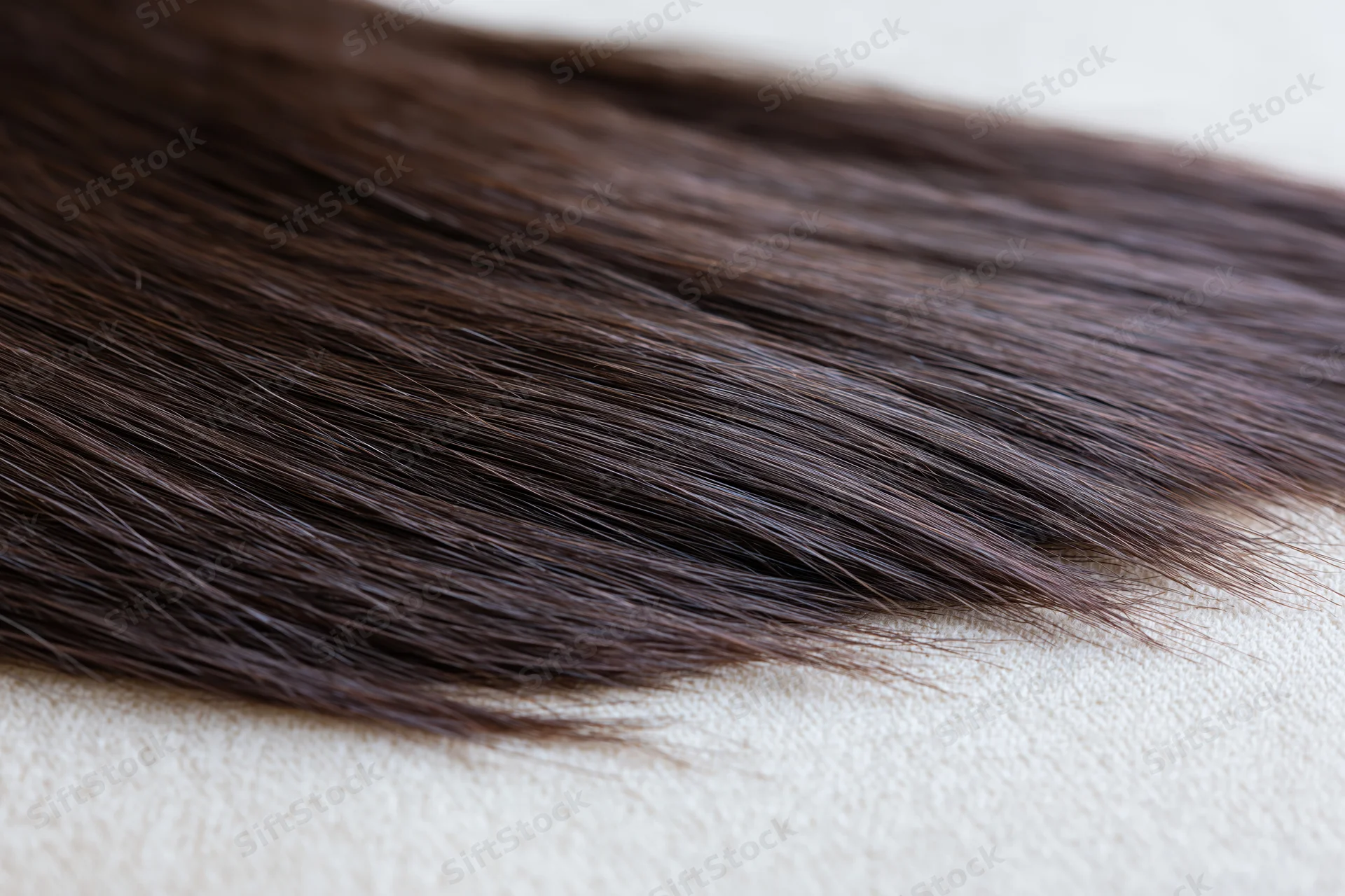 Close-up of dark brown hair extension lying on a textured surface
