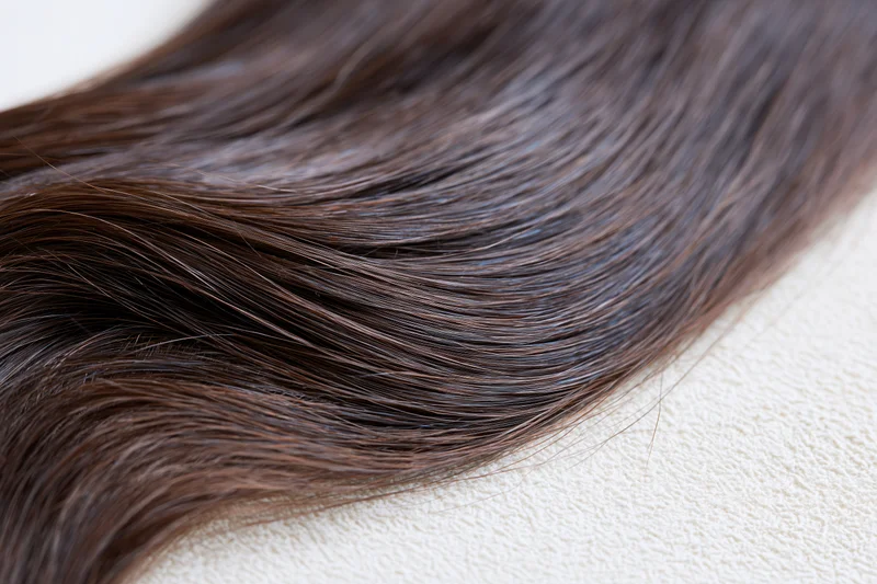 Close-up of dark brown hair extension lying on a textured surface