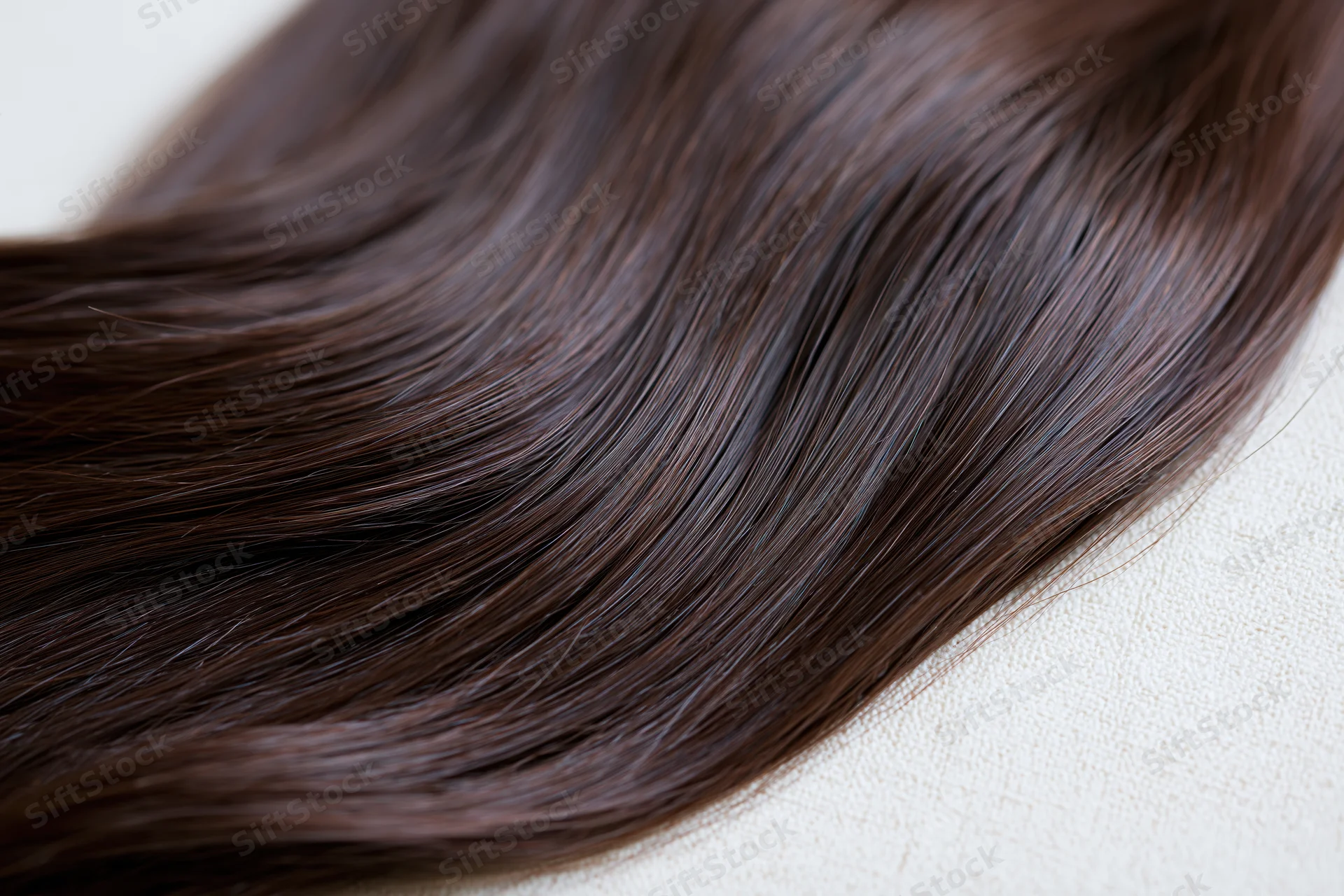 Close-up of dark brown hair extension lying on a light fabric surface