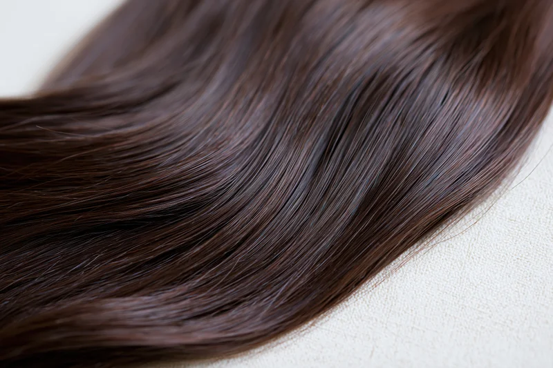 Close-up of dark brown hair extension lying on a light fabric surface