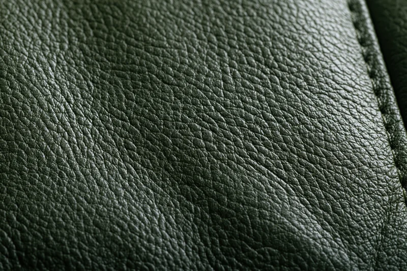 Close-up of dark forest green leather surface with visible grain and stitching