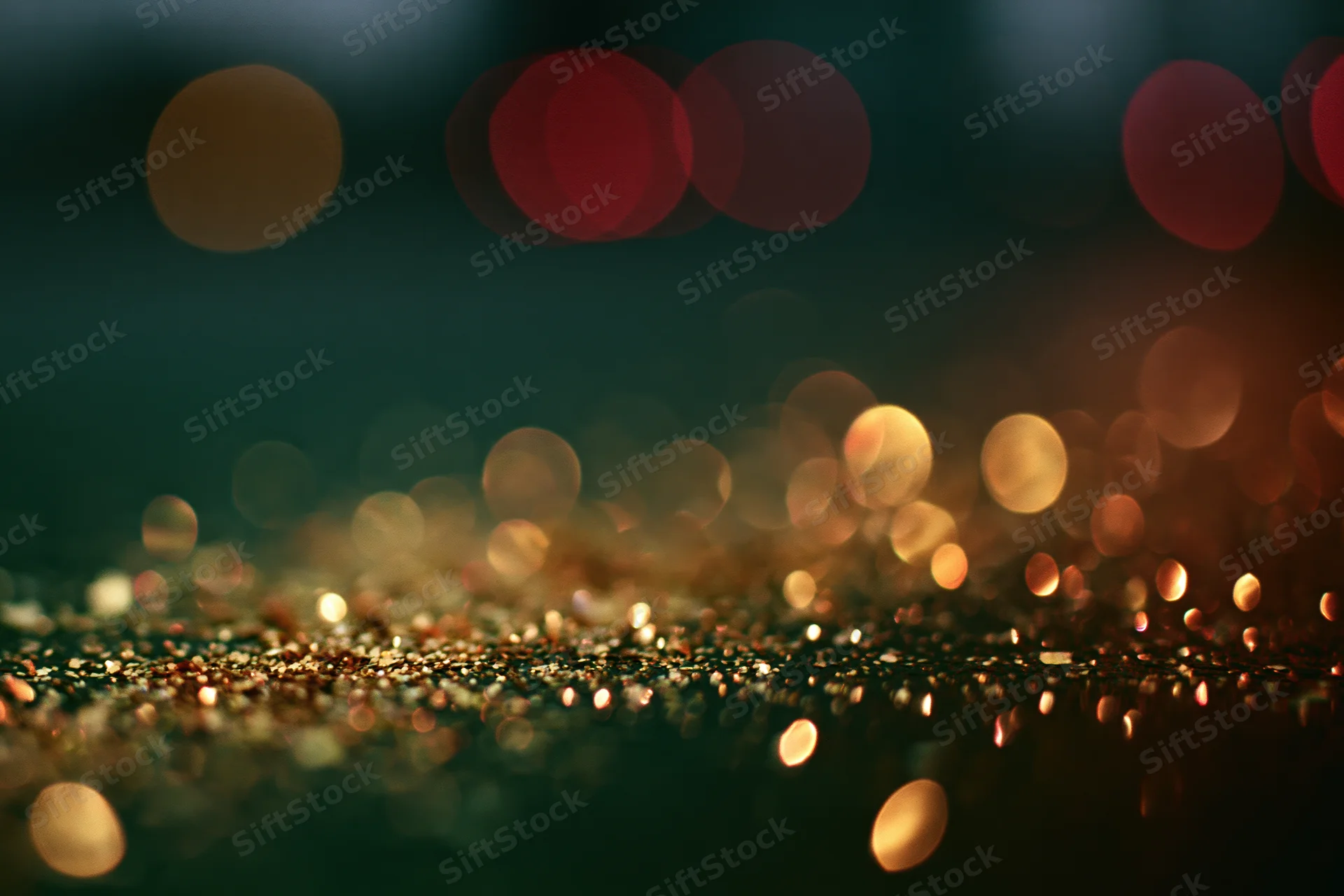 Scattered gold glitter particles on a dark surface with bokeh lights in the background