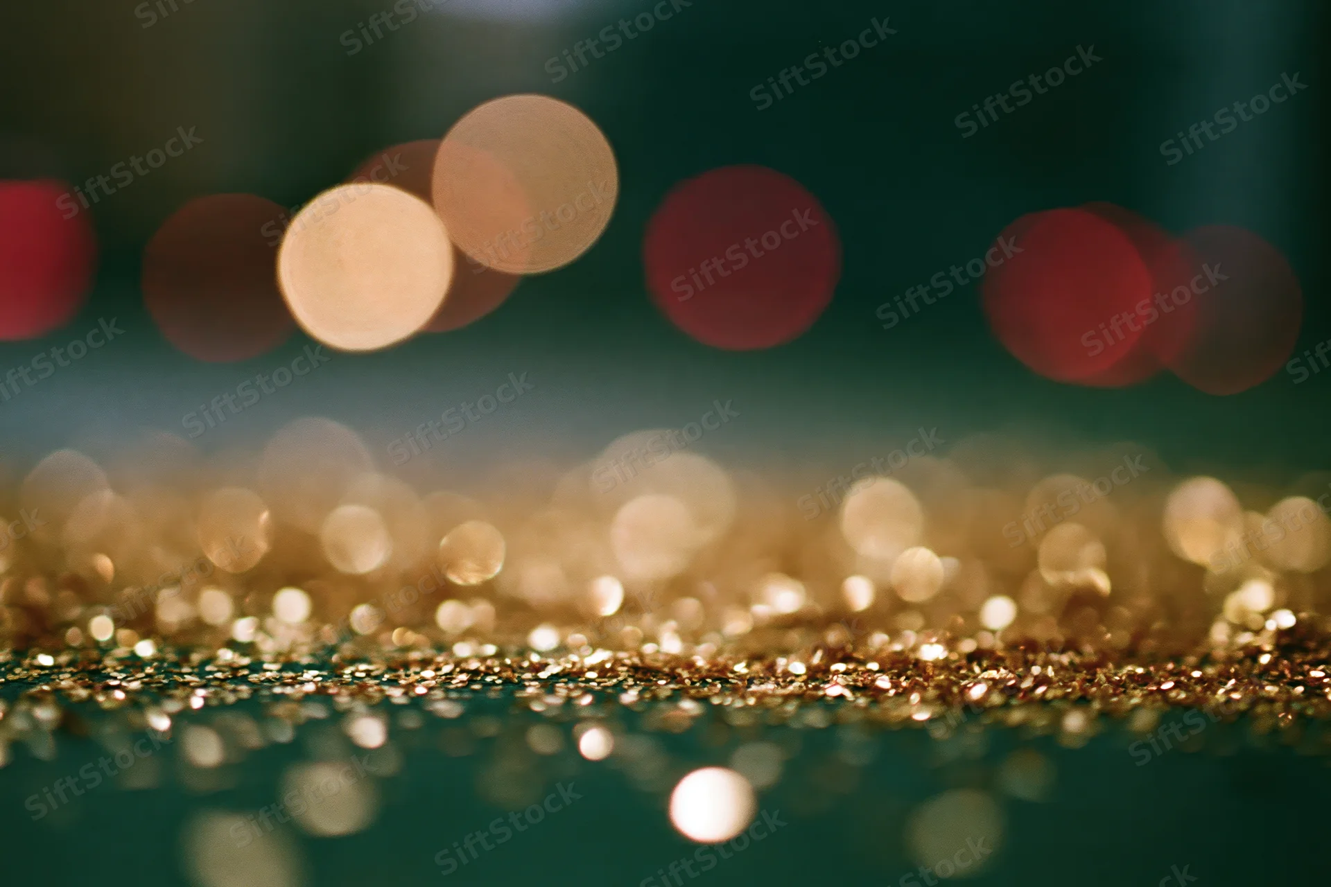 Scattered gold glitter particles on a dark surface with blurred bokeh lights in the background