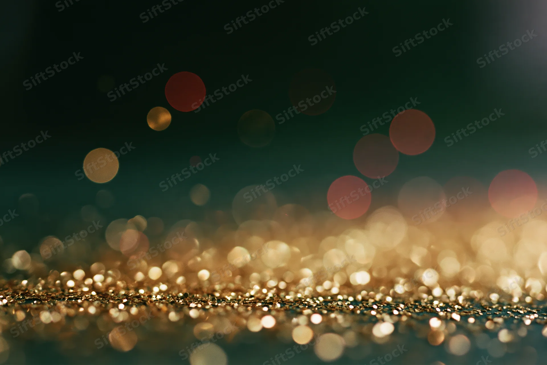 Scattered gold glitter particles on a dark surface with bokeh lights in the background