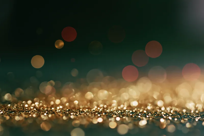 Scattered gold glitter particles on a dark surface with bokeh lights in the background