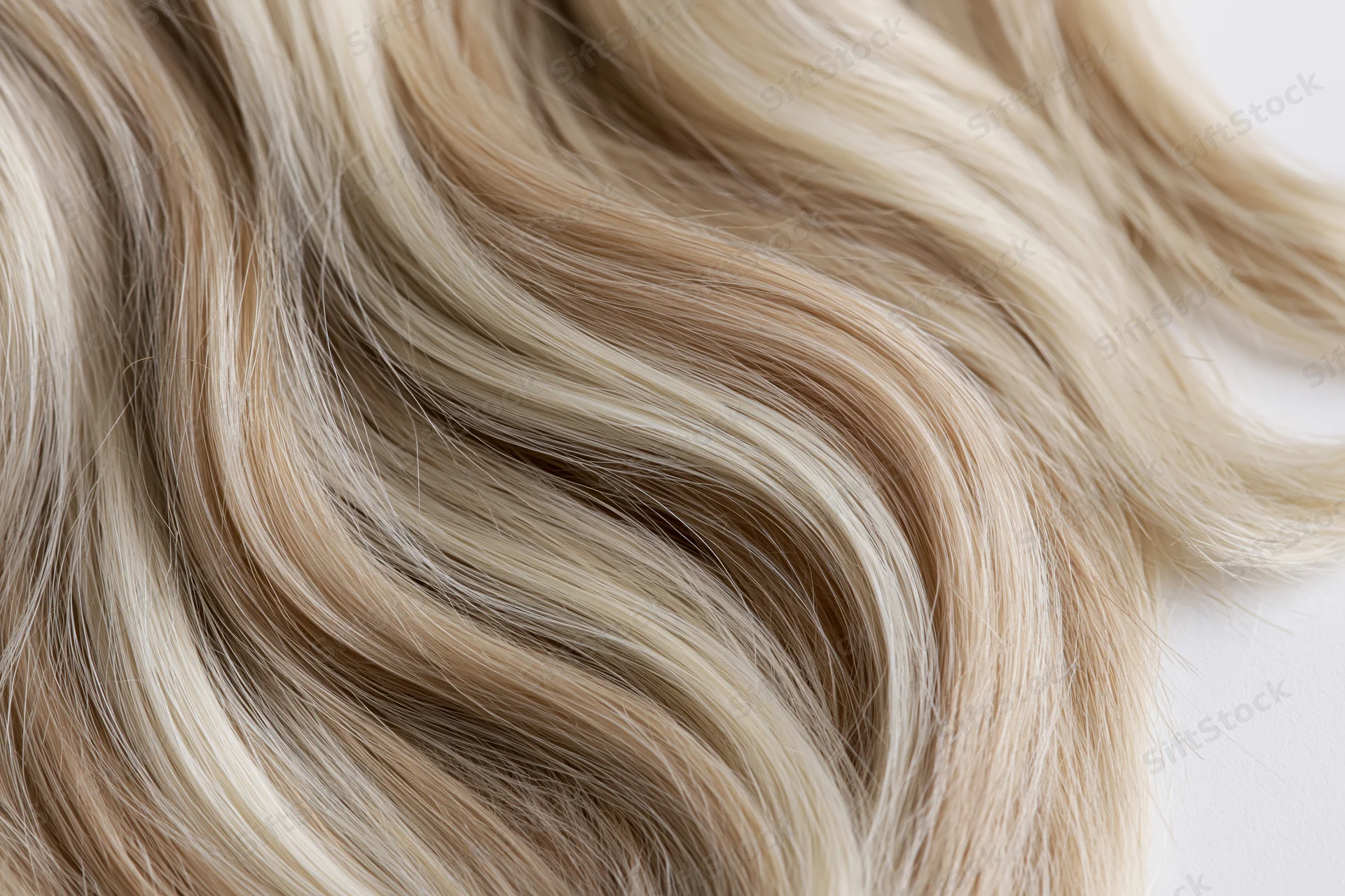 Close-up of wavy blonde hair strands laid flat on a white surface