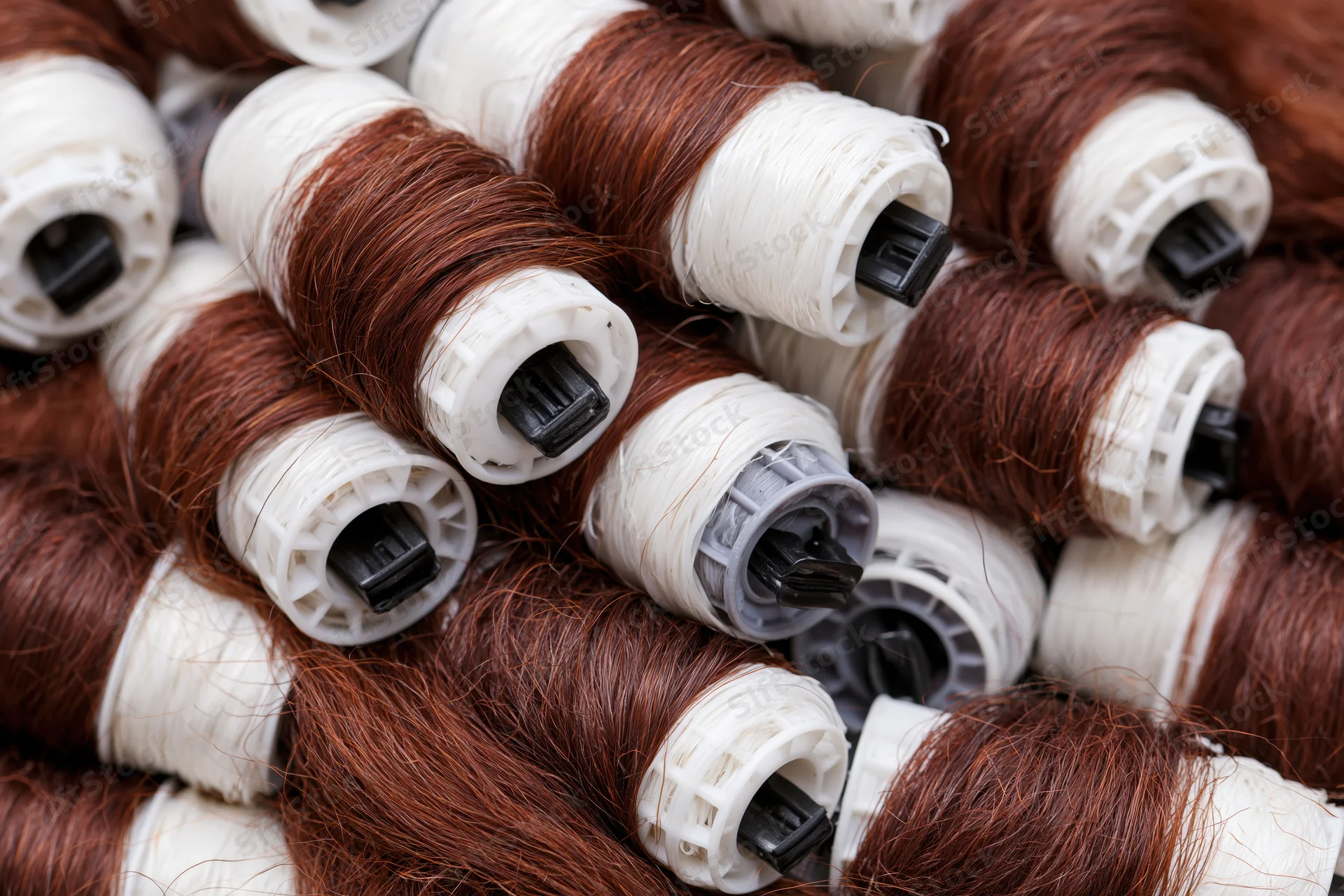 Close-up of auburn brown synthetic hair extensions wound on white plastic spools in a pile