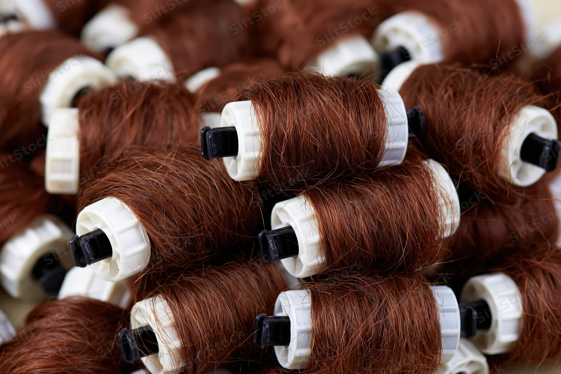 Auburn synthetic hair extensions wound on white plastic spools stacked closely together