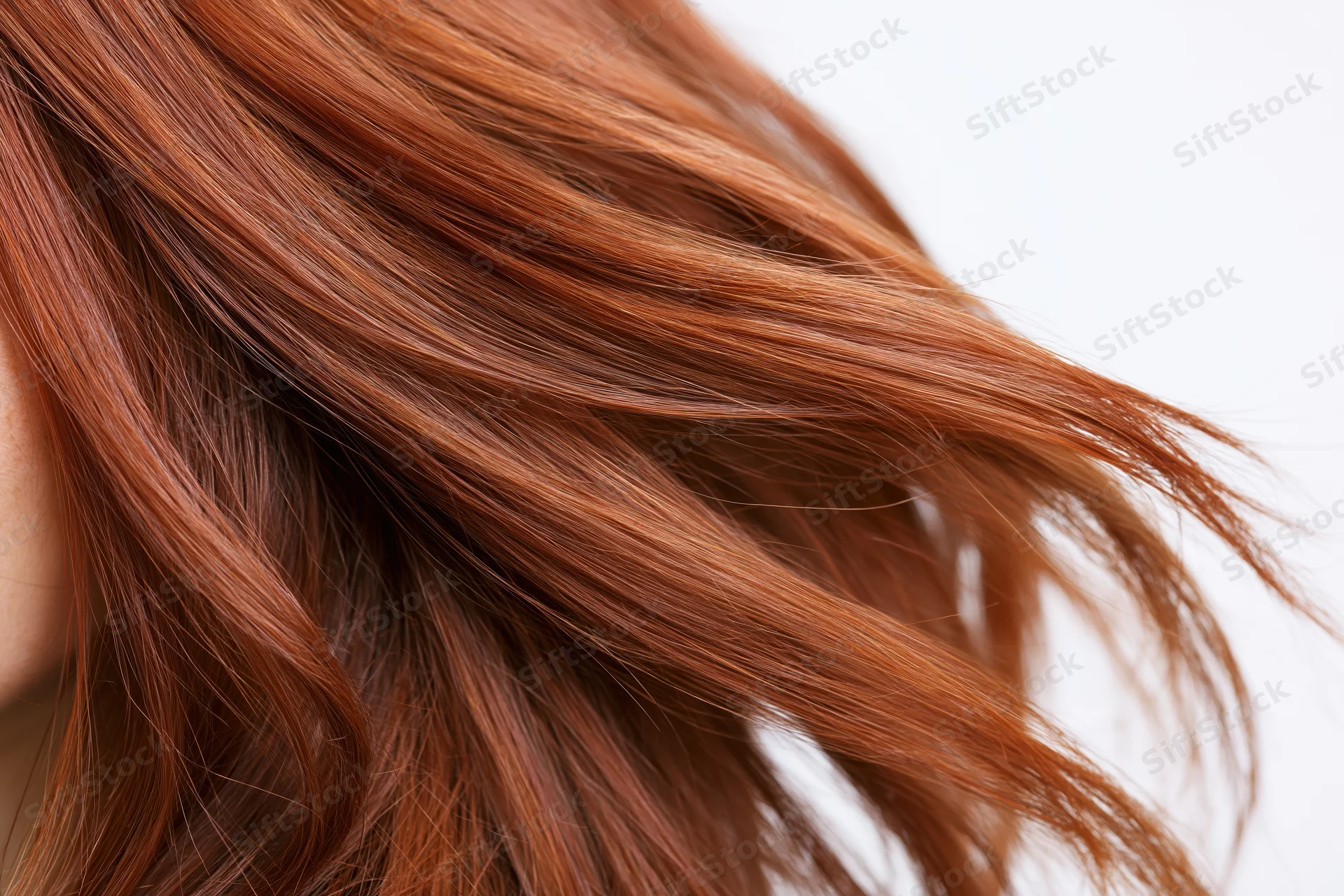 Close-up of flowing auburn red hair strands curving mid-motion against white background