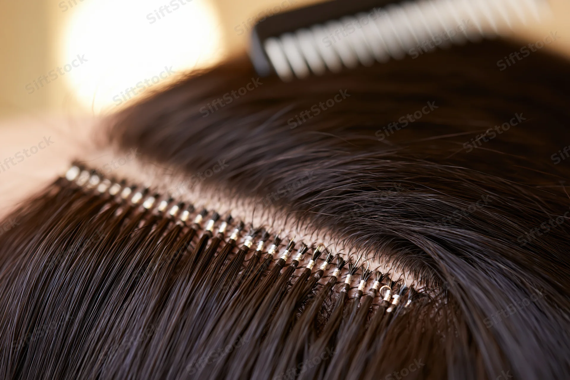 Close-up of hair extensions bonded along a section of scalp with a comb nearby