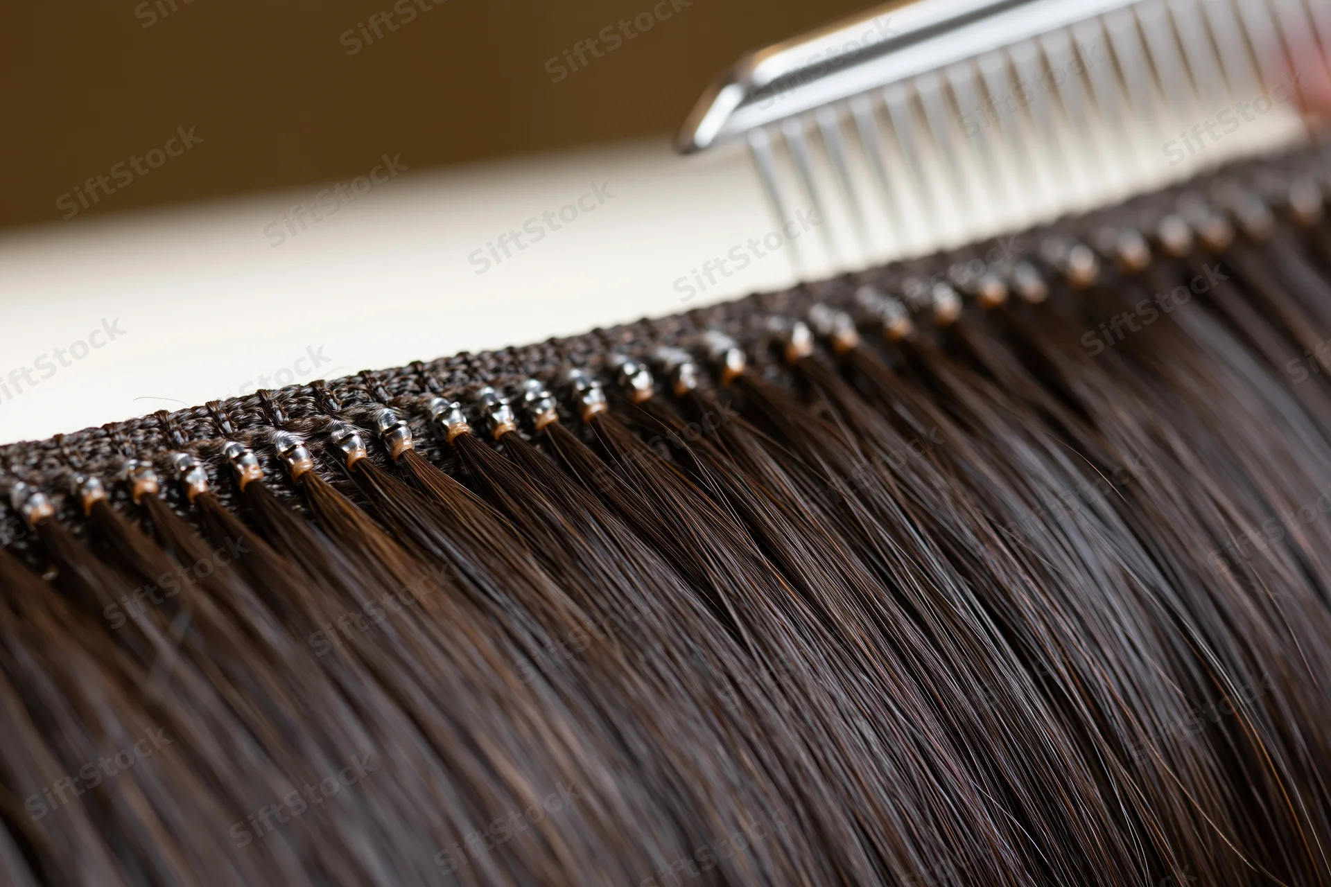 Close-up of dark hair extensions with bonds along a weft being combed