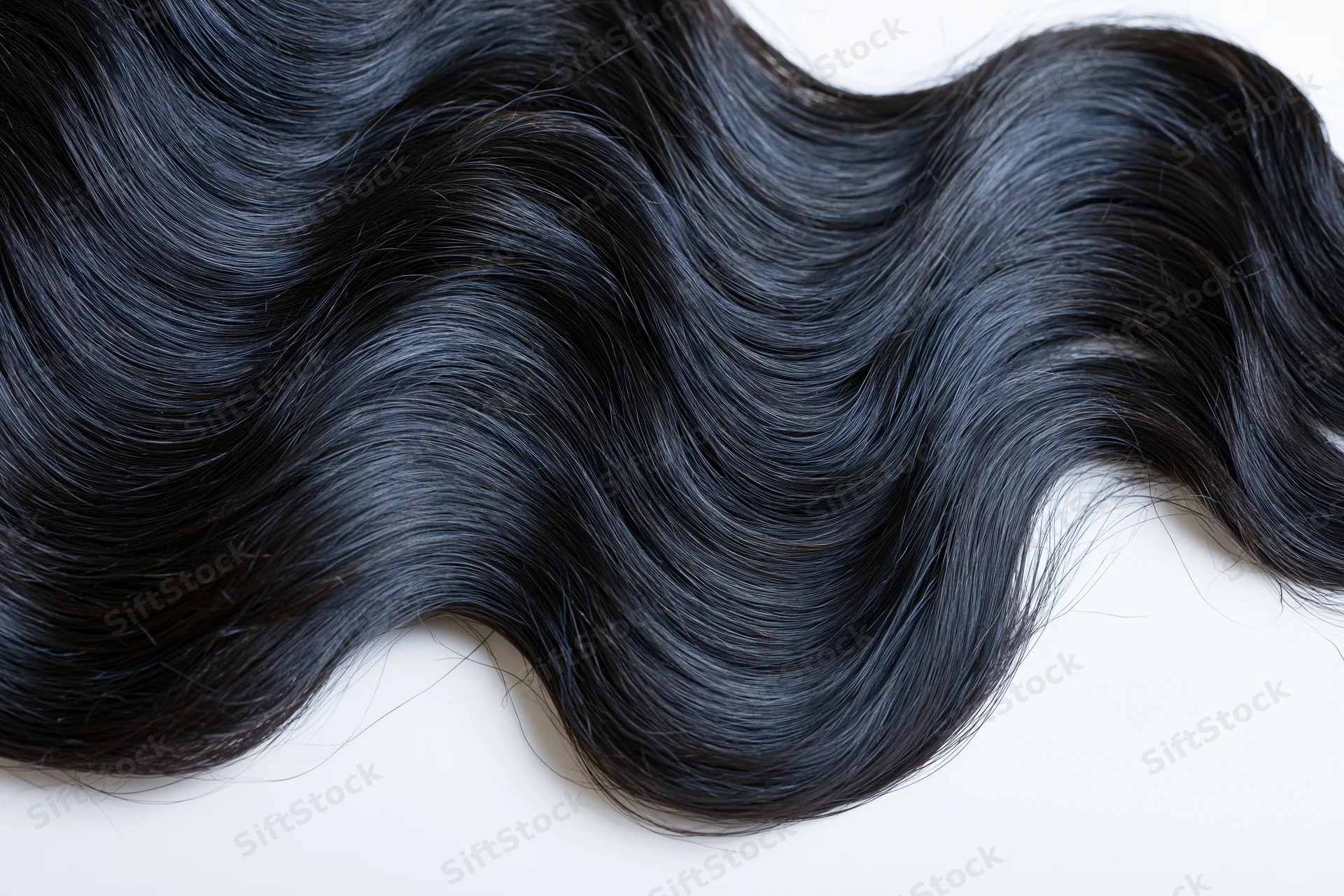 Close-up of long glossy black wavy hair spread across a clean white surface
