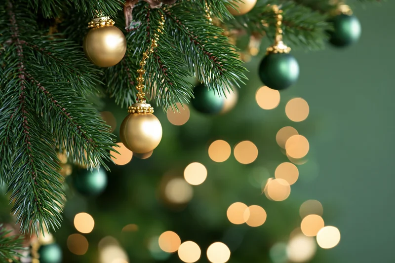 Close-up of pine branches with gold and green ornaments and blurred lights in the background