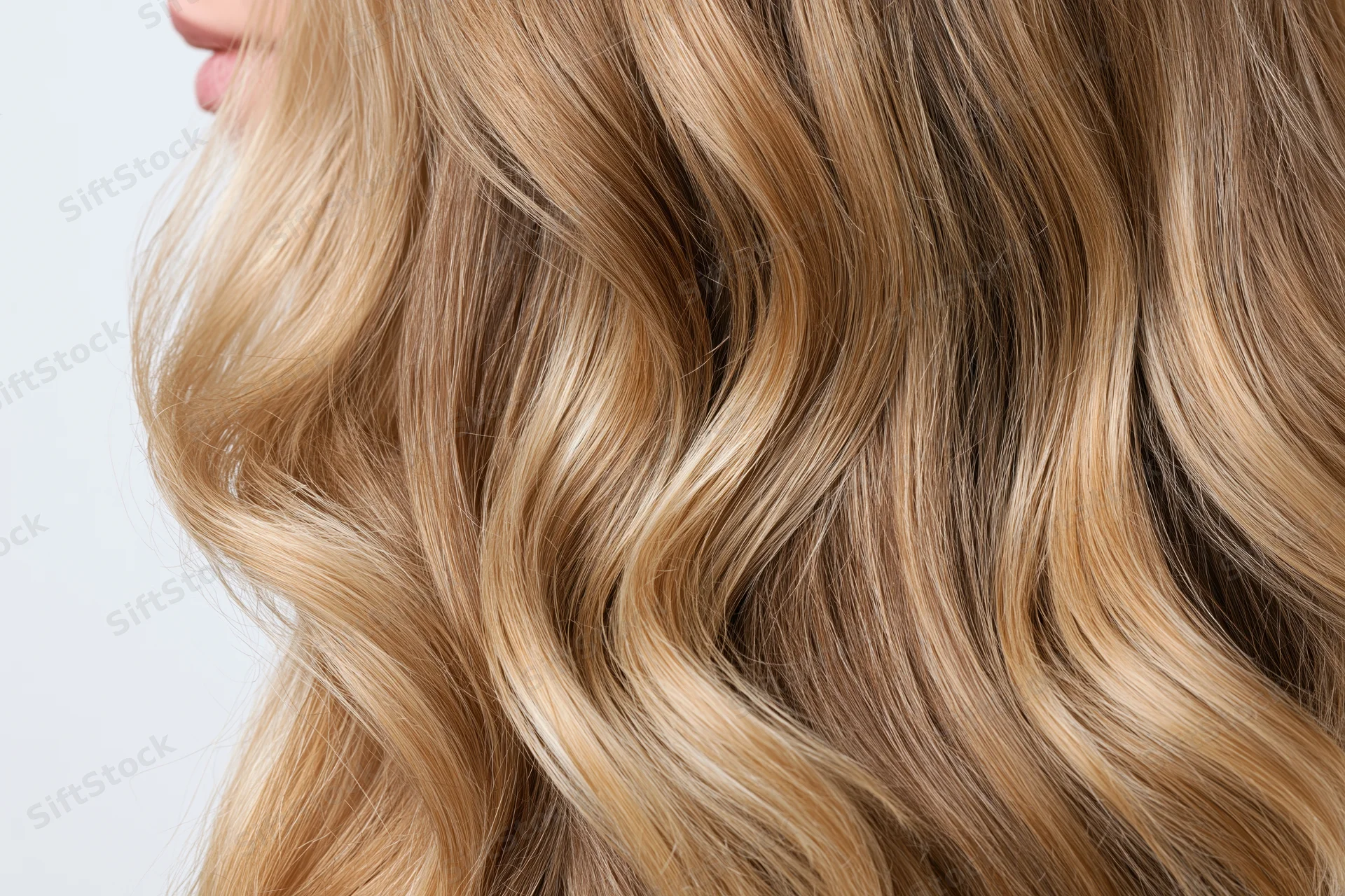 Close-up of thick wavy blonde hair with natural highlights on a woman's head against a plain background