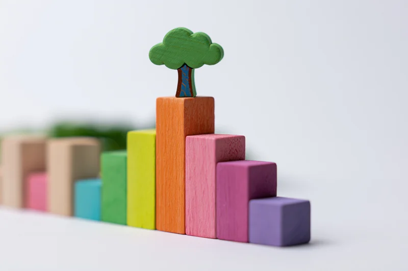 Colorful wooden blocks arranged in ascending bar chart with tree on top against white background