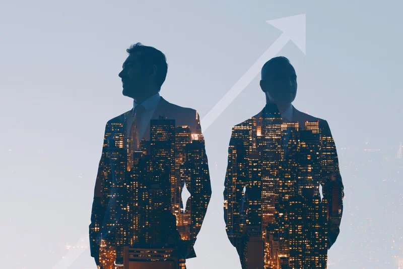 Two business professionals in silhouette with city skyline double exposed inside their suits, showing upward growth arrow in background