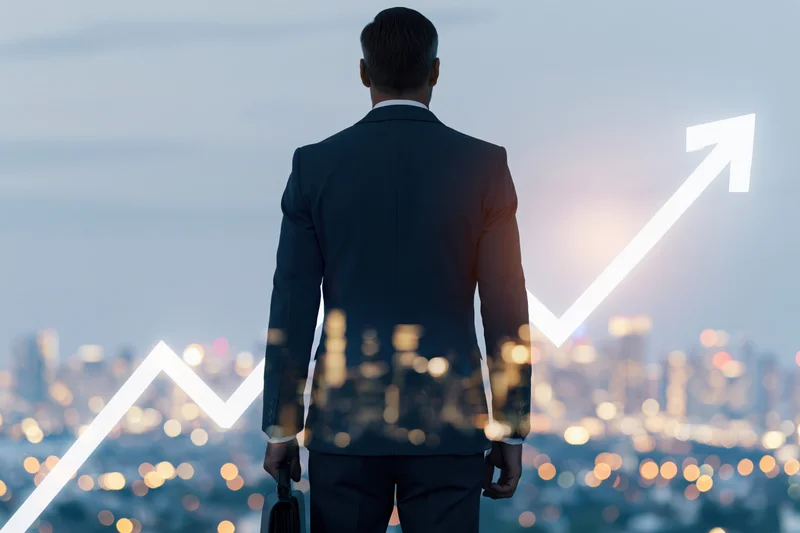 Businessman in suit standing with cityscape and upward arrow overlay, back view
