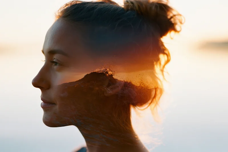 Double exposure portrait of a young woman’s profile with mountain landscape overlay at sunset