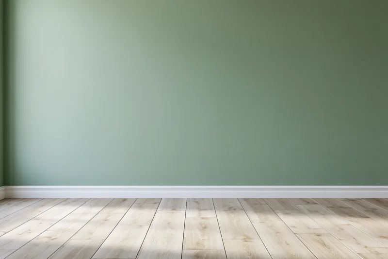 Empty room with sage green painted wall and light wooden floor, featuring white baseboard and natural light