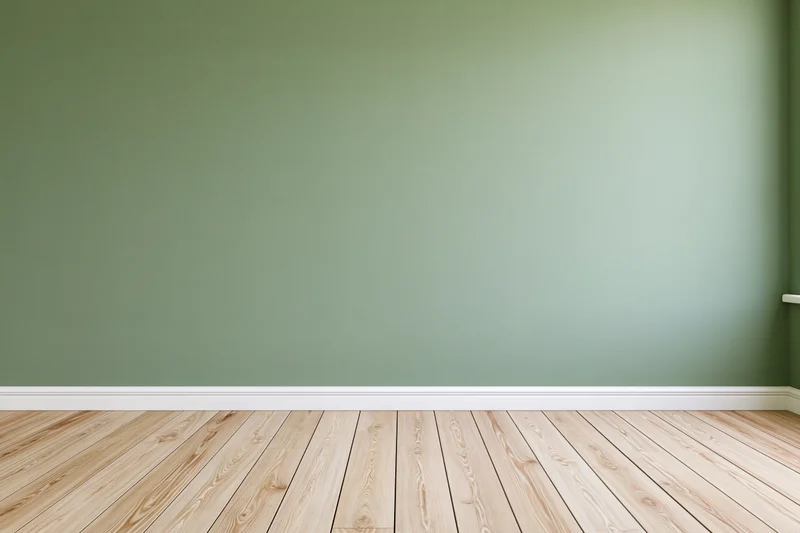Empty room with sage green painted wall and wooden floor, featuring white baseboard and corner view