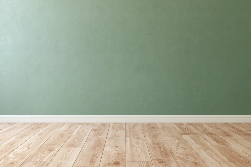 Empty room with sage green painted wall and wooden floor, white baseboard, minimalist interior space