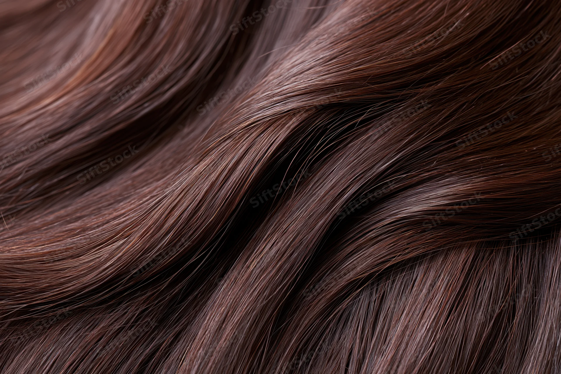 Closeup of dark brown human hair strands showing smooth texture and natural waves