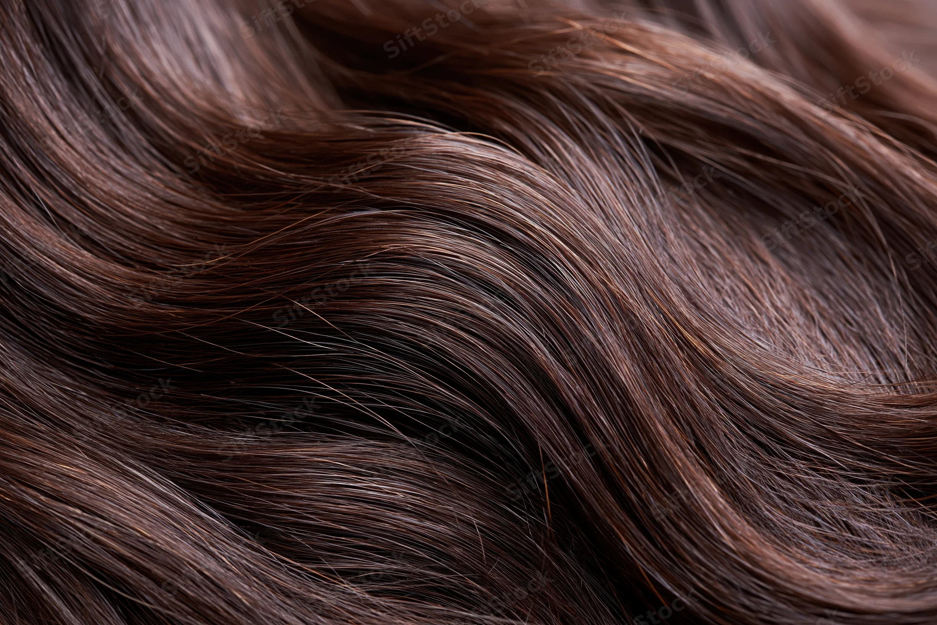 Closeup of dark brown human hair strands showing glossy texture and natural waves