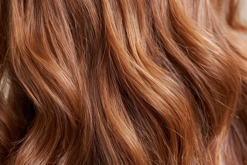 Closeup of wavy auburn hair with natural highlights and glossy texture