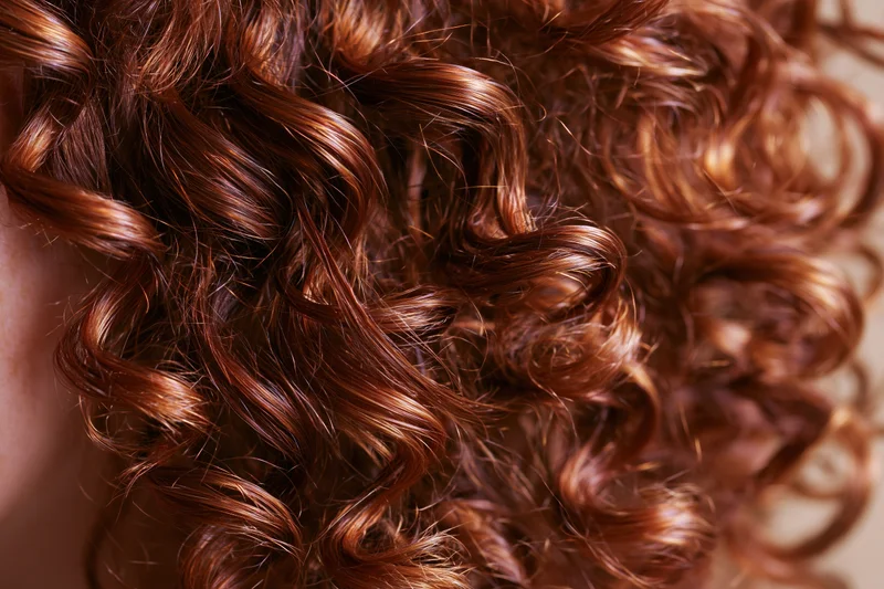 Close-up of natural curly auburn hair with glossy texture and volume