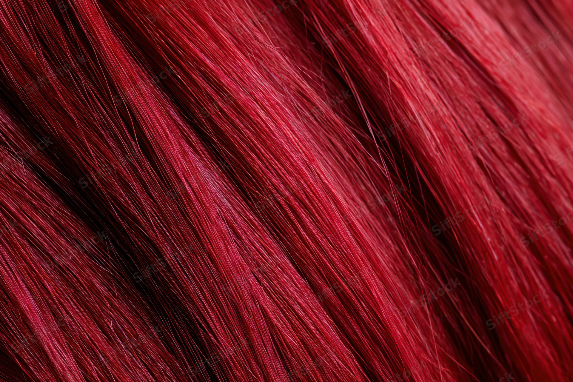 Extreme close-up of vibrant red dyed human hair strands showing glossy texture