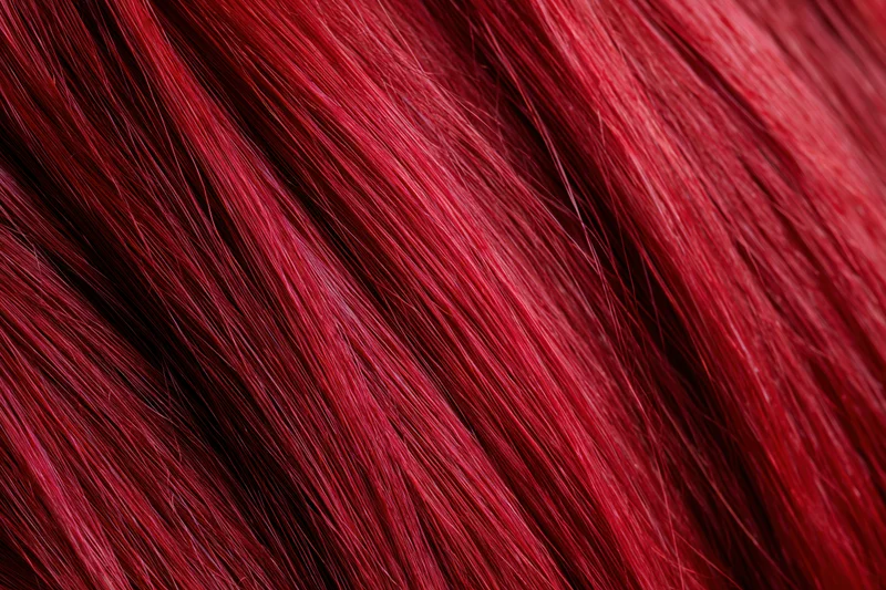 Extreme close-up of vibrant red dyed human hair strands showing glossy texture
