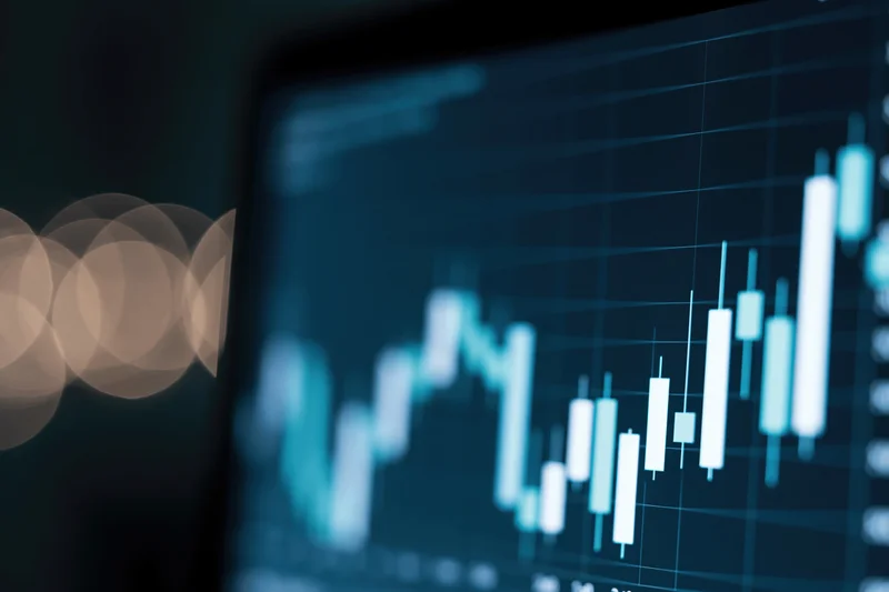 Financial candlestick chart on a dark digital screen with blurred lights in the background