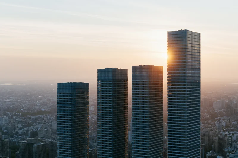 Five modern glass skyscrapers rising in ascending height against a sunset cityscape