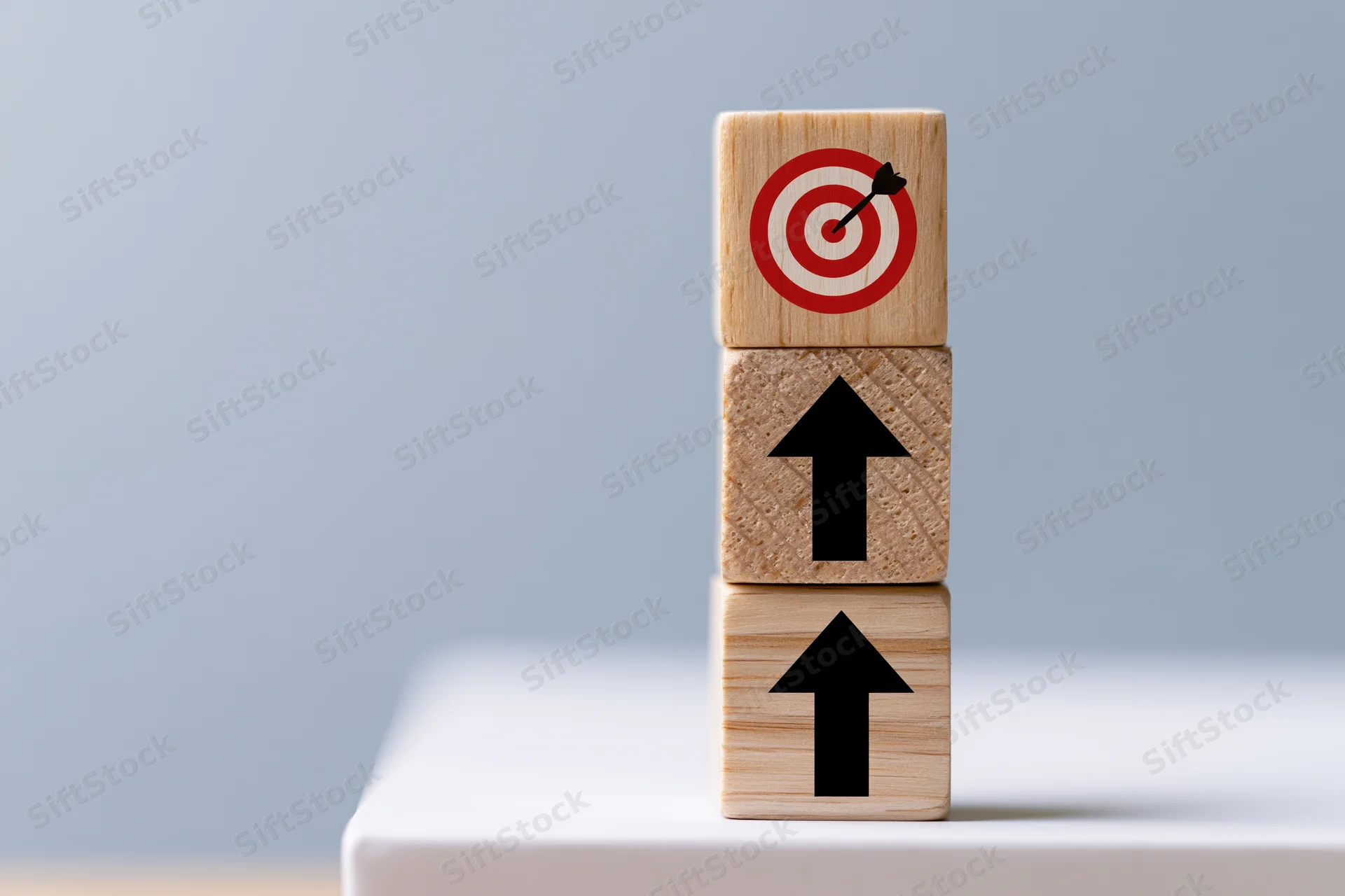 Three wooden cubes stacked vertically with upward arrows and a target on top on a white surface