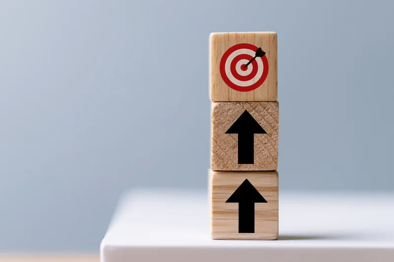Three wooden cubes stacked vertically with upward arrows and a target on top on a white surface