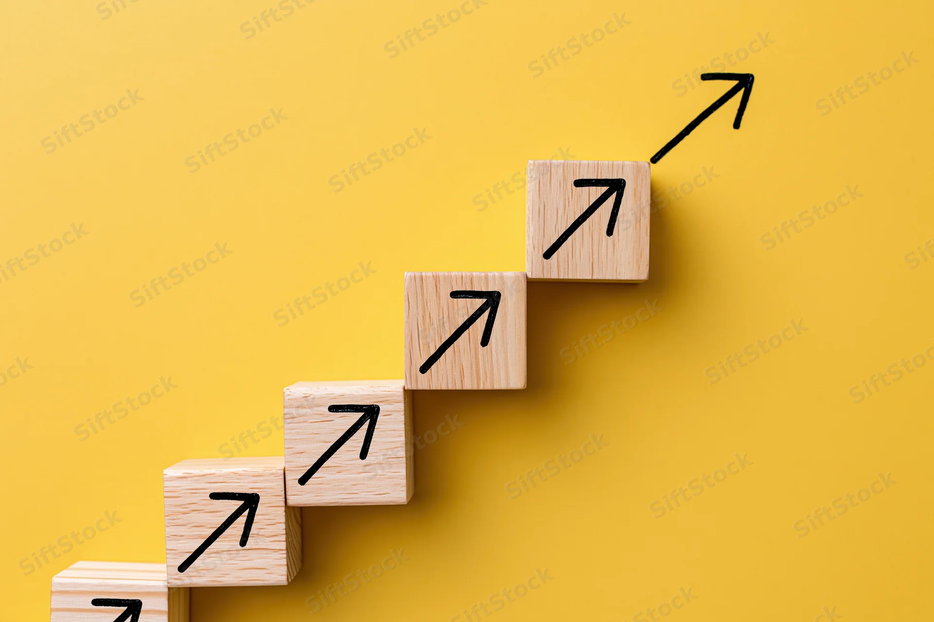 Wooden blocks with arrows arranged in ascending steps on yellow background