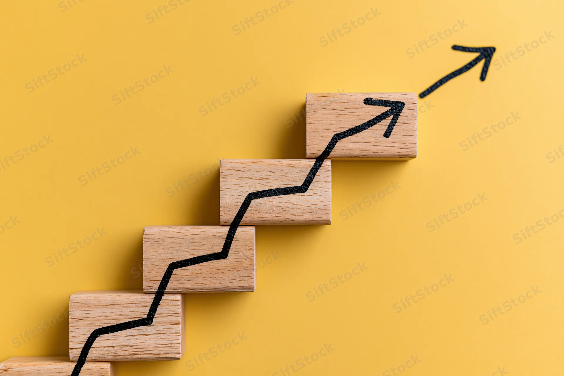 Wooden blocks arranged in ascending steps with a black arrow tracing upward growth on a yellow background