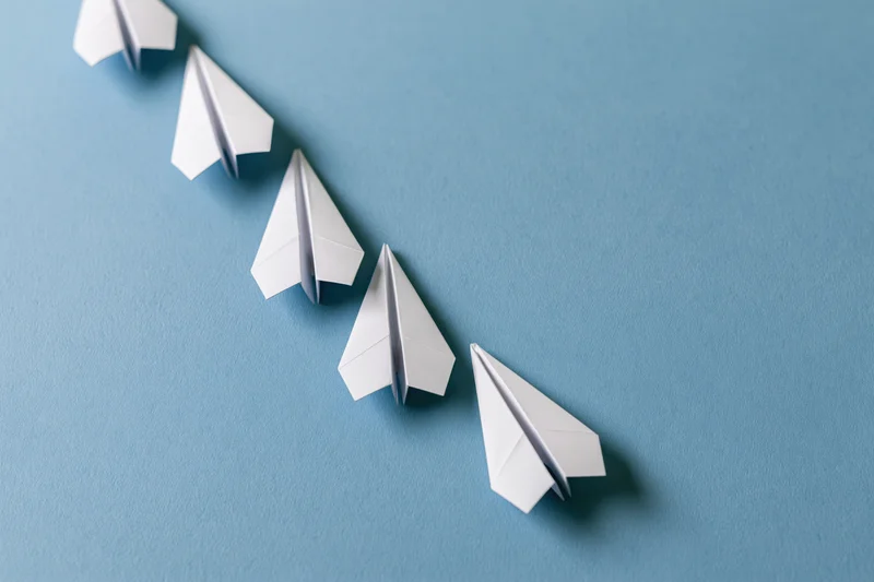 Five white paper airplanes arranged diagonally in ascending order on a blue surface