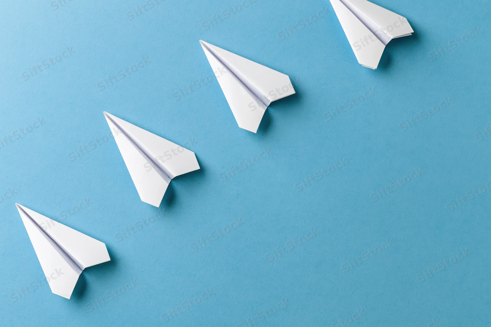 Five white paper airplanes arranged diagonally ascending on a blue surface