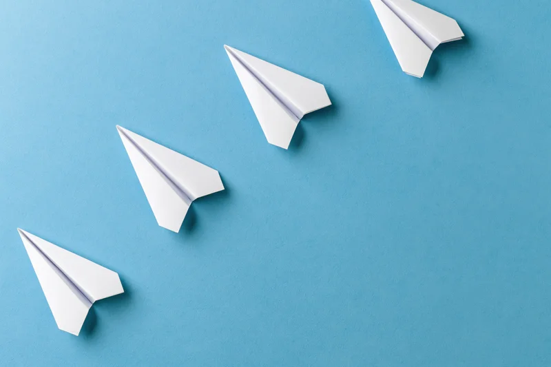 Five white paper airplanes arranged diagonally ascending on a blue surface