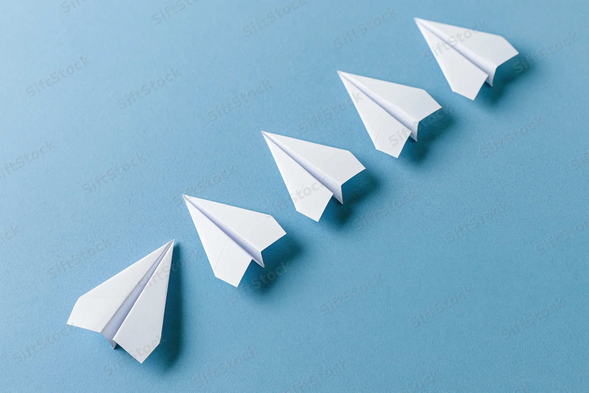 Five white paper airplanes arranged diagonally in ascending order on a blue surface
