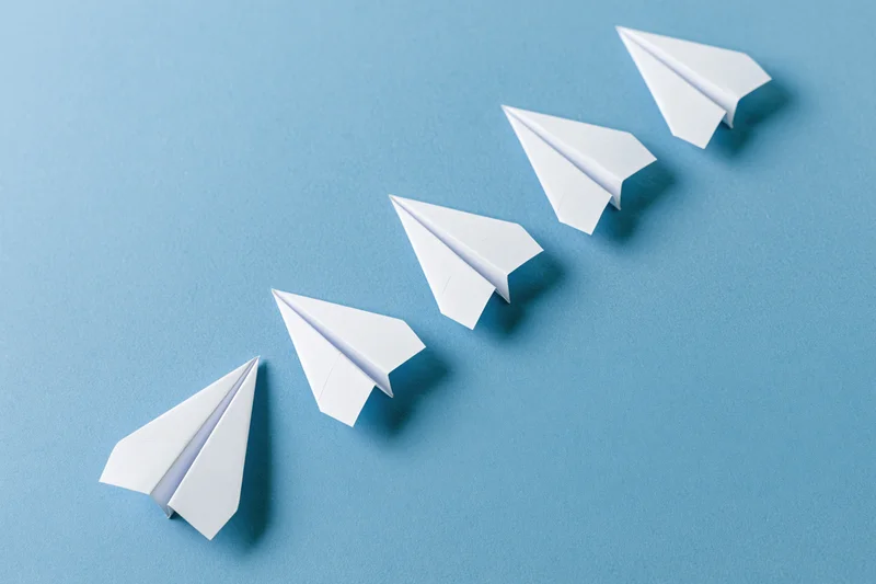 Five white paper airplanes arranged diagonally in ascending order on a blue surface