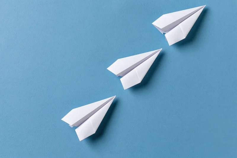 Three white paper airplanes arranged diagonally ascending on a blue surface
