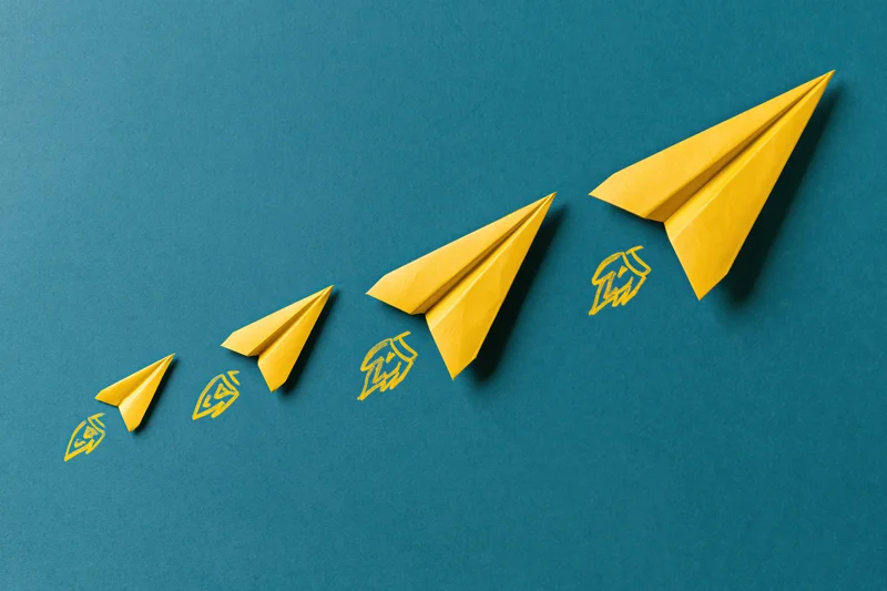Five yellow paper airplanes arranged in a rising diagonal line on blue background