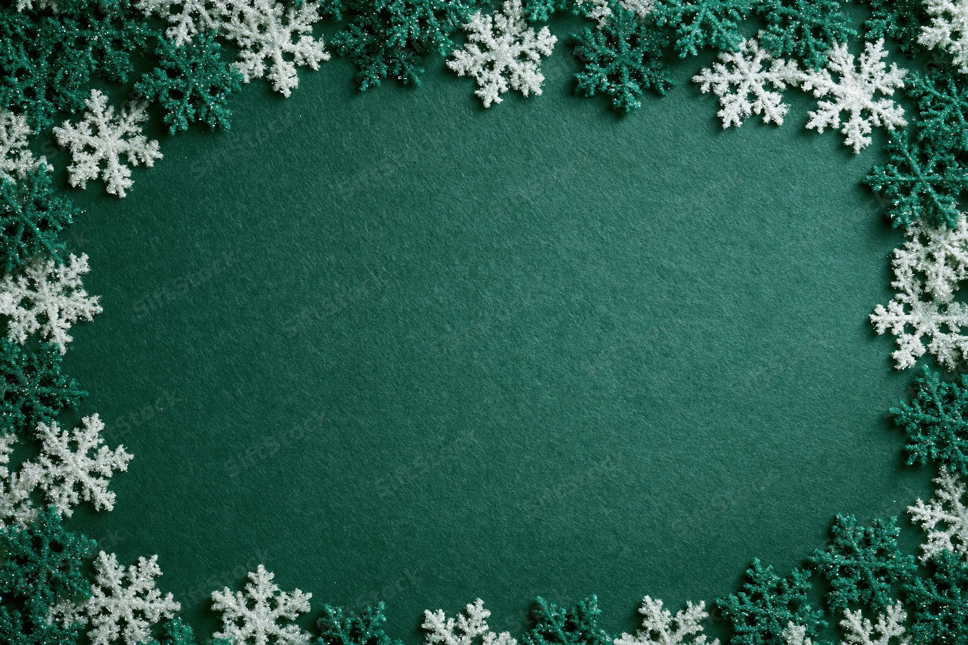 Snowflakes arranged in a border around a green textured surface creating a festive holiday frame with copyspace