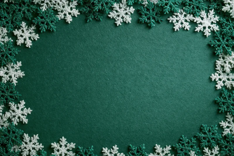Snowflakes arranged in a border around a green textured surface creating a festive holiday frame with copyspace
